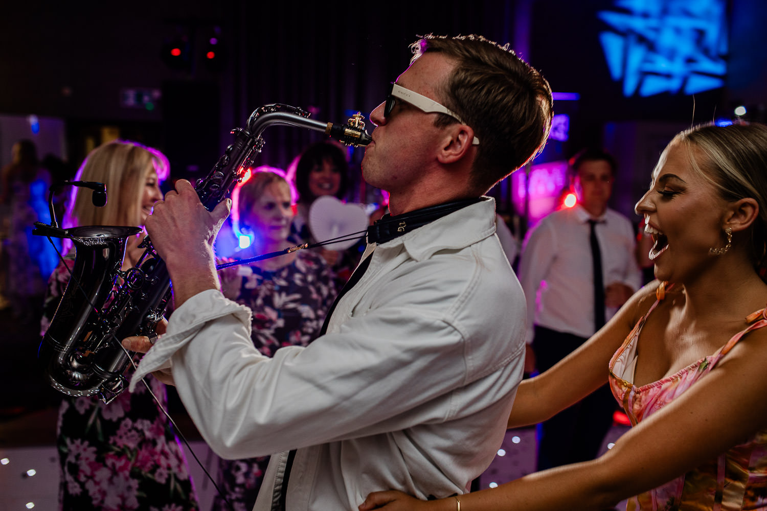 Daniel Costin Sax playing the saxophone in a conga line on the dancefloor at wedding reception.