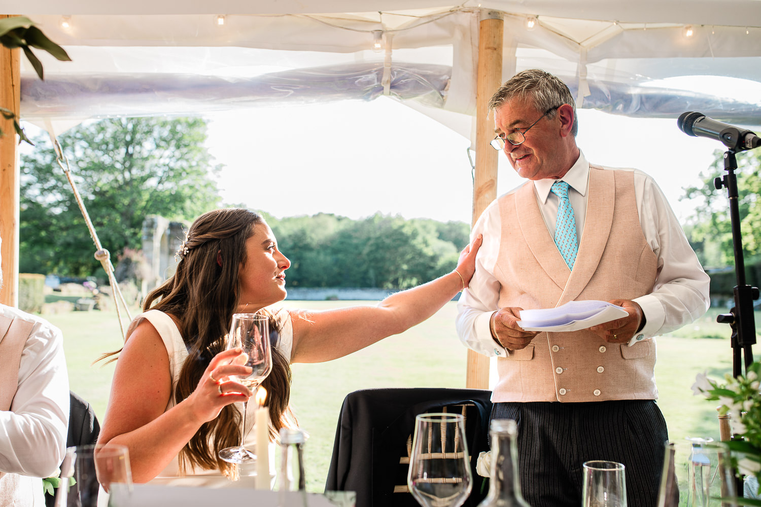 A candid moment shared between a bride and her father, after a wedding speech during a marquee wedding reception in England.