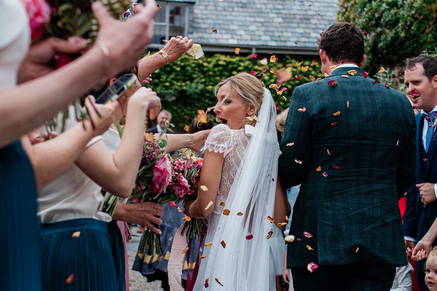 A bride looks back at her friend in surprise during a confetti shot at The Great Barn wedding venue.