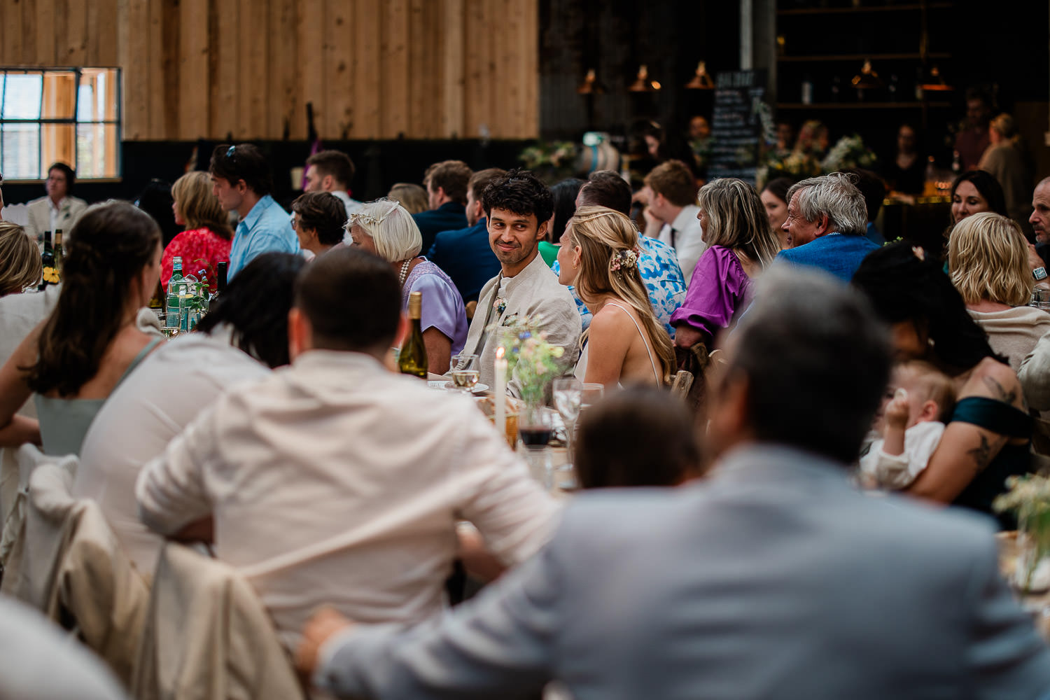 Bride and groom share loving look, whilst surrounded by guests at an English barn reception.