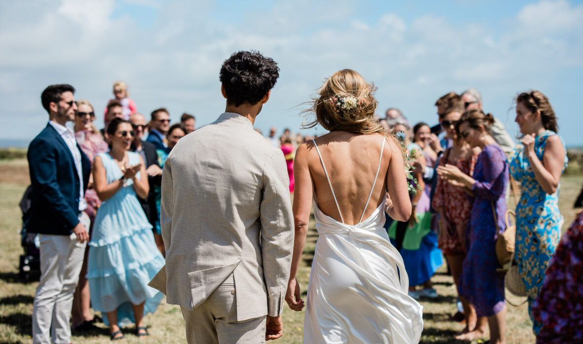 A bride and groom look back at their wedding guests at their bohemian inspired seaside wedding, after an outdoor confetti shot.