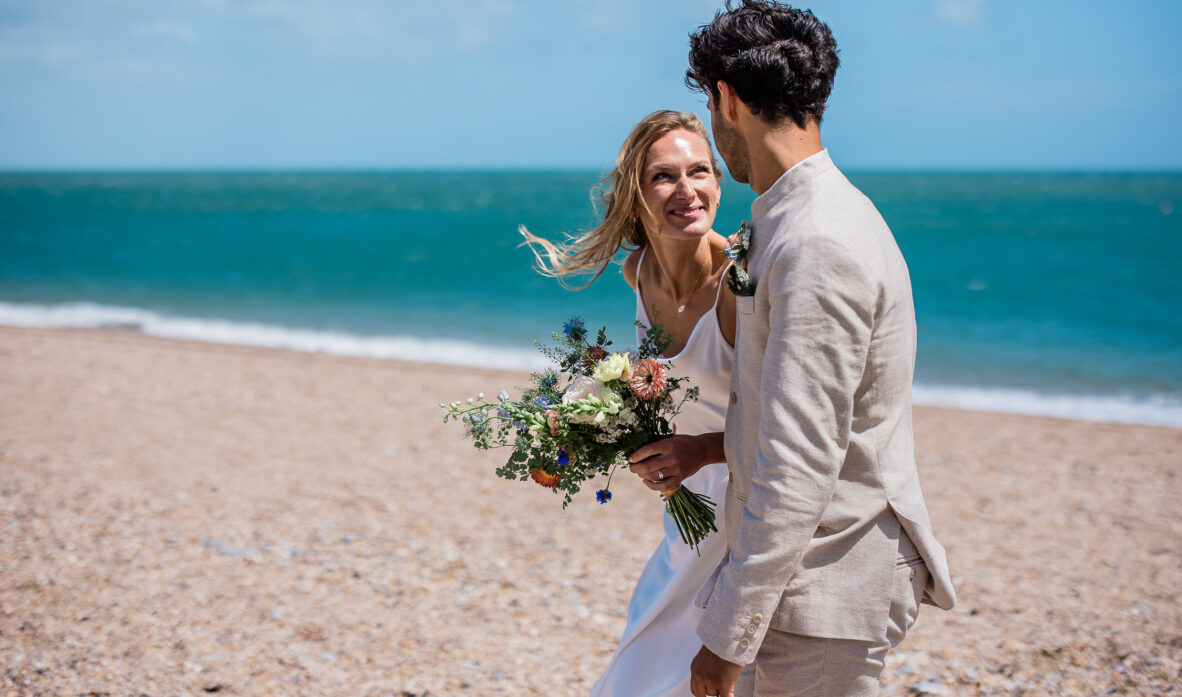 A bride smiles up at the groom, whilst taking a walk on the beach during their english seaside wedding reception in Devon.