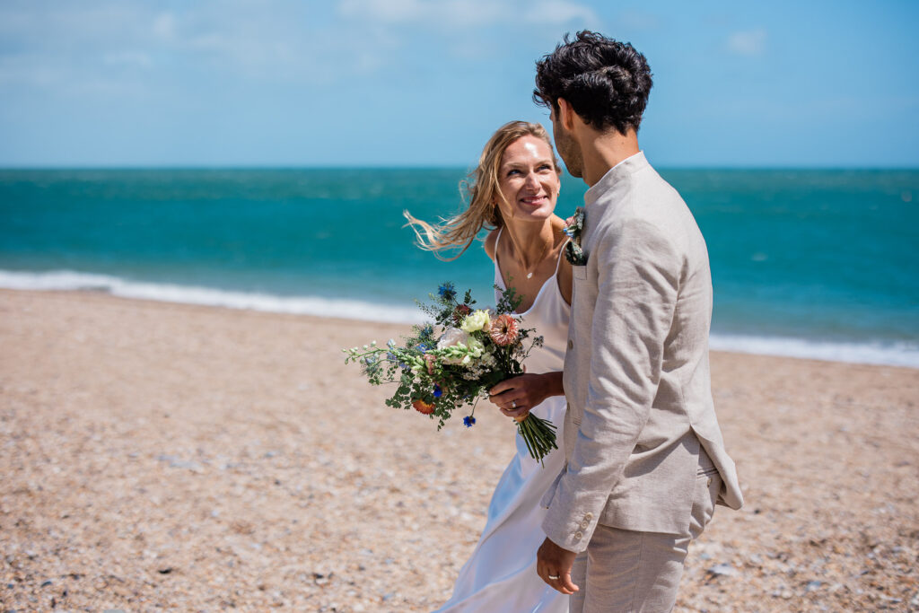 A bride smiles up at the groom, whilst taking a walk on the beach during their english seaside wedding reception in Devon.